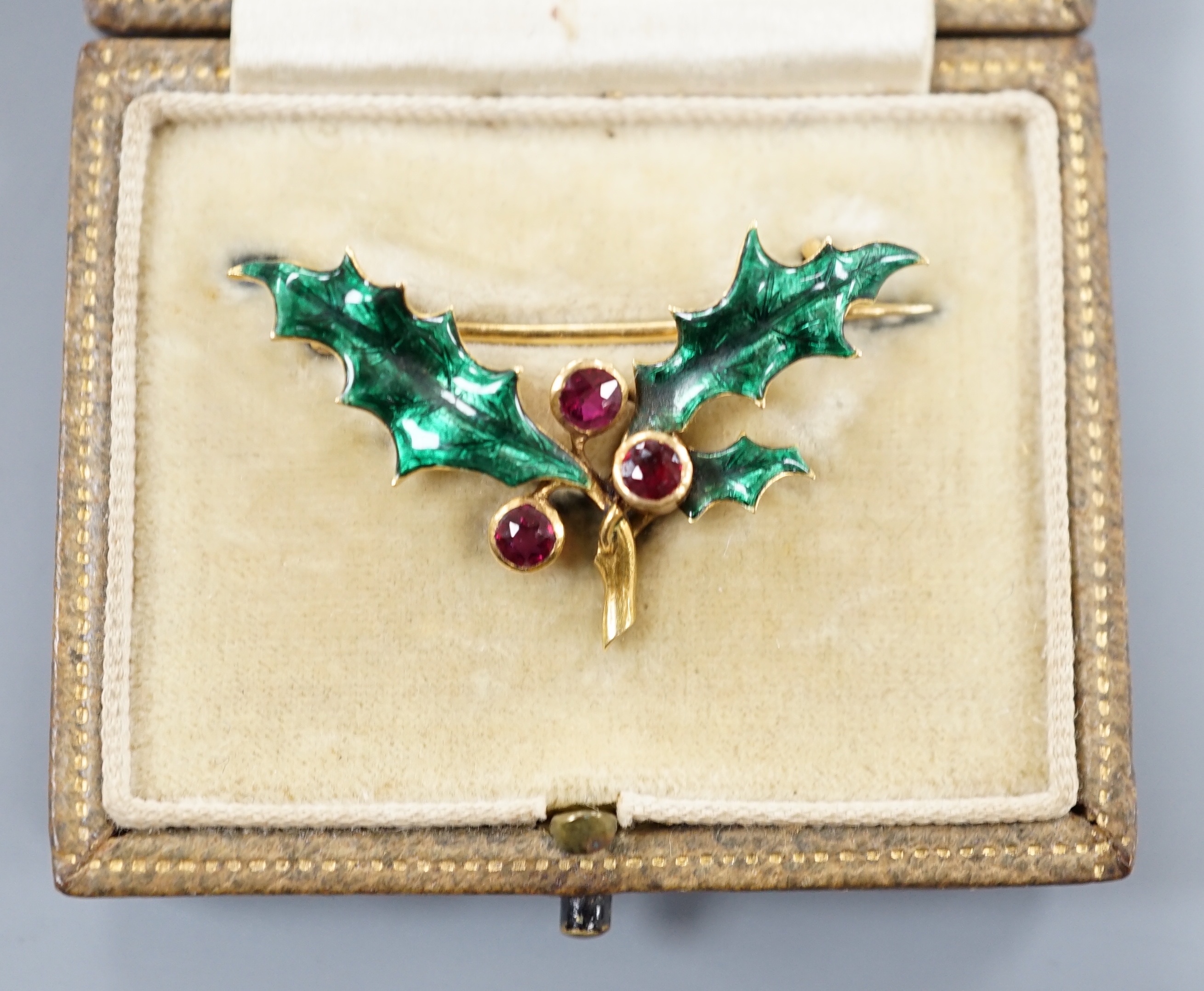 A cased yellow metal, ruby and green enamel set 'holly and berry' brooch, 36mm, gross weight 5 grams.